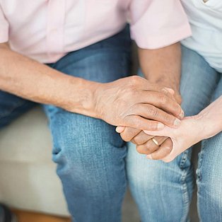 Eine Person sitzt neben einer anderen und hält tröstend ihre Hand.