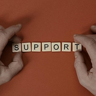 Zwei Hände legen mit Scrabble-Spielsteinen das Wort "Support".