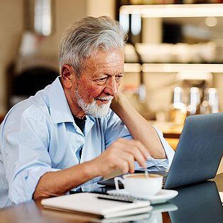 Älterer Mann schaut in einem Café interessiert vor seinem Laptop.