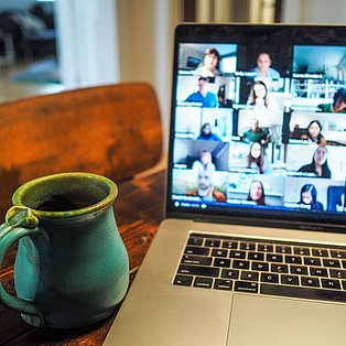 Videokonferenz auf dem Bildschirm eines Laptops, davor eine Tasse